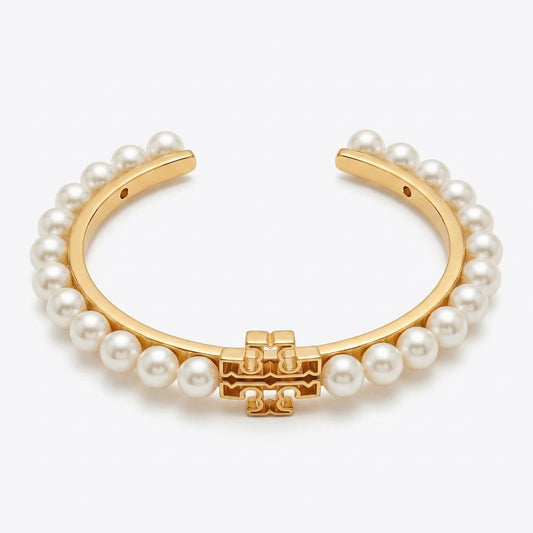 A gold-plated cuff bracelet adorned with a row of white faux pearls and a central gold-tone geometric charm, shown on a light gray background.