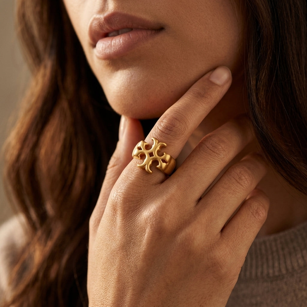 A close-up lifestyle shot of a woman wearing a textured gold ring on her finger, with her hand resting near her chin.