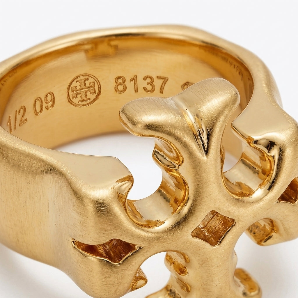 Close-up of a gold ring with an abstract, organic sculptural design and engraved interior markings including a circular monogram and size number 8.