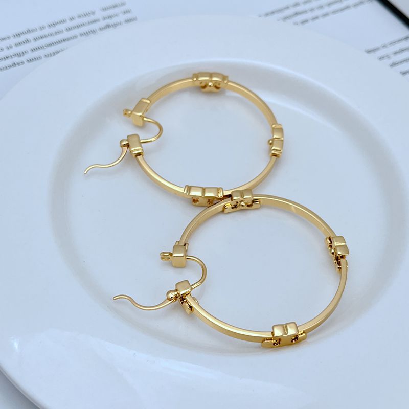 : "Extreme close-up of the iconic intertwined Serif Double T logo charm on the gold hoop earring, highlighting exquisite craftsmanship."