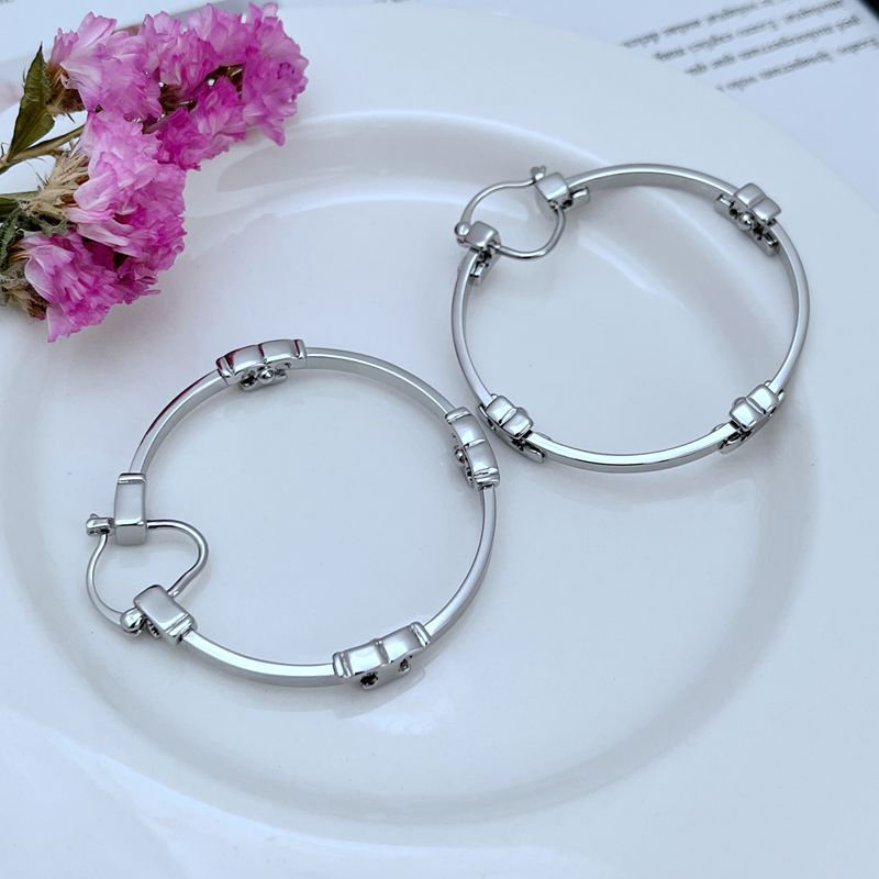 : "Extreme close-up of the iconic intertwined Serif Double T logo charm on the gold hoop earring, highlighting exquisite craftsmanship."