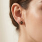 A close-up of a person's ear wearing a small black enamel cross stud earring.