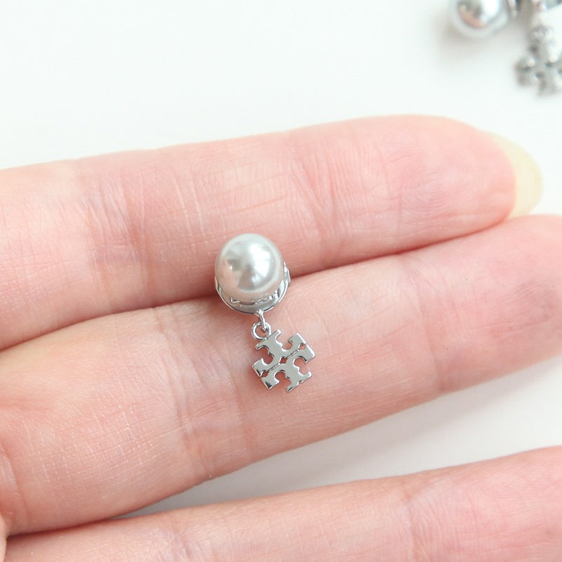 A silver stud earring with a white pearl and a dangling puzzle piece charm, shown resting on a person's fingers against a white background.