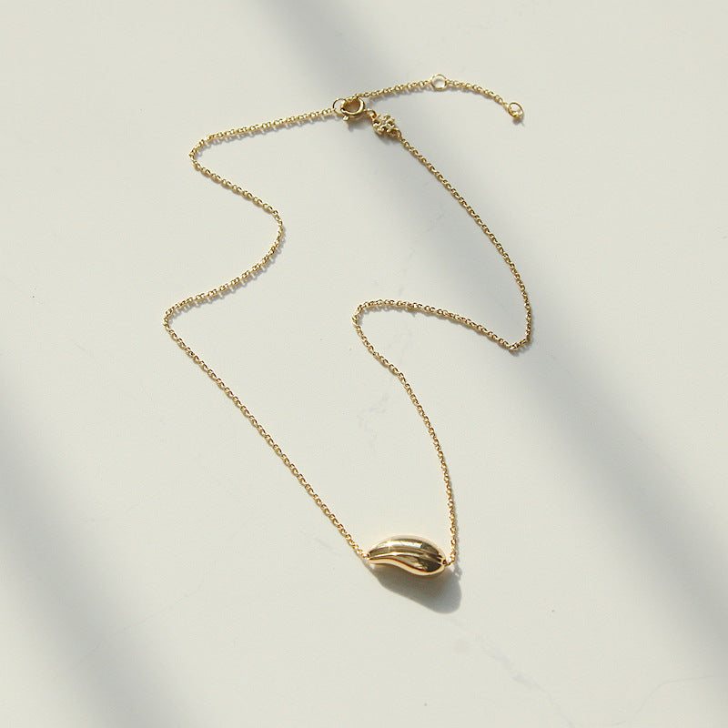 A delicate gold chain necklace with a small, polished gold leaf pendant, laid out on a light off-white surface with soft shadows.