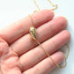 A gold teardrop-shaped pendant necklace resting on a person's hand against a light background.