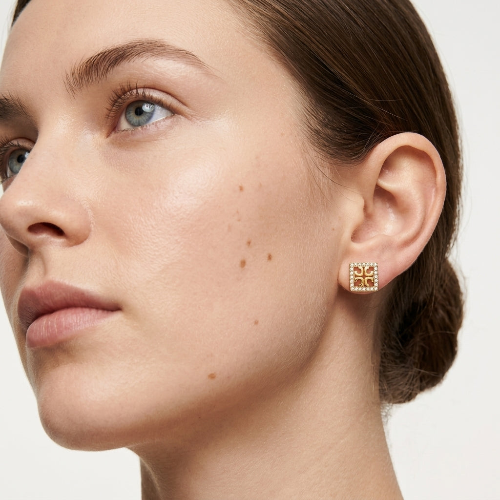 Close-up of a woman wearing gold square earrings on a neutral background