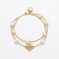 A double-strand gold chain bracelet with freshwater pearls and a central gold cross charm embellished with small clear crystals, shown on a plain white background.