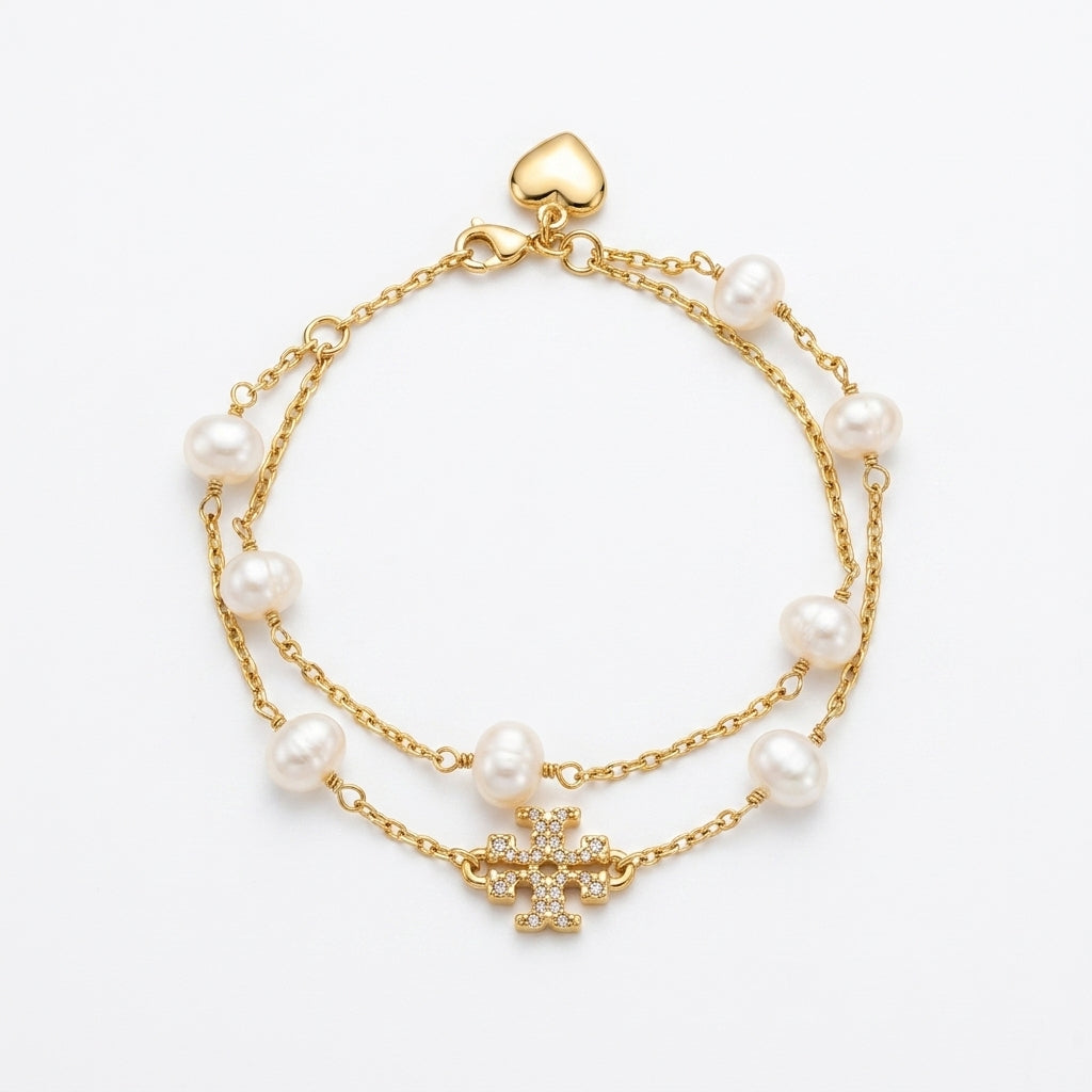 A double-strand gold chain bracelet with freshwater pearls and a central gold cross charm embellished with small clear crystals, shown on a plain white background.