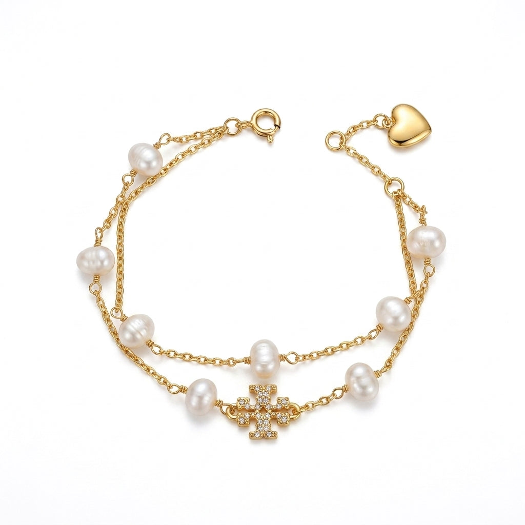 A gold-tone double-strand chain bracelet featuring white freshwater pearls, a central pavé cross charm, and an adjustable heart-shaped clasp, shown on a plain white background.