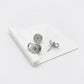 A pair of silver-toned stud earrings displayed on a white folded card against a clean white background. One earring is shown from the front with a circular cutout design, and the other is turned to show the post and backing.