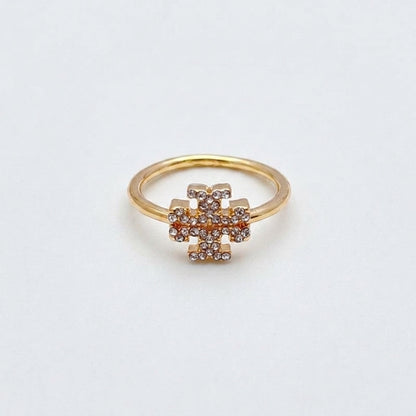 A gold ring with a central geometric cluster of small clear stones, photographed on a plain light background.