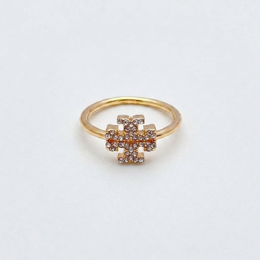 A gold ring with a central geometric cluster of small clear stones, photographed on a plain light background.