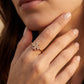 A close-up of a woman's hand wearing a delicate gold ring with a small cluster of clear stones in a floral or snowflake-like setting.