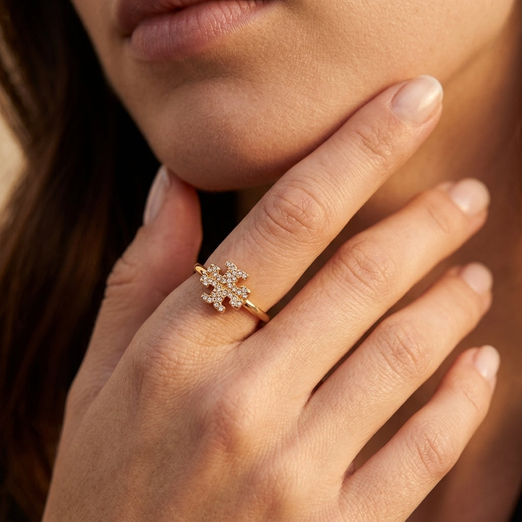 A close-up of a woman's hand wearing a delicate gold ring with a small cluster of clear stones in a floral or snowflake-like setting.
