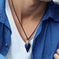 Person wearing a blue shirt with a necklace featuring a silver pendant.