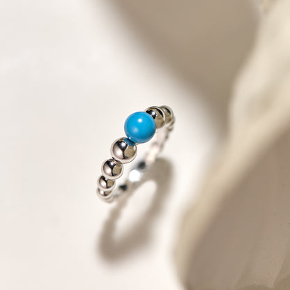 Silver ring with a blue bead on a light background