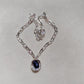  Necklace on neutral or jewel-tone background. Alt: “UNO de 50 Short Link Chain Pendant Necklace with Purple Crystal.”