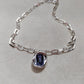  Necklace on neutral or jewel-tone background. Alt: “UNO de 50 Short Link Chain Pendant Necklace with Purple Crystal.”
