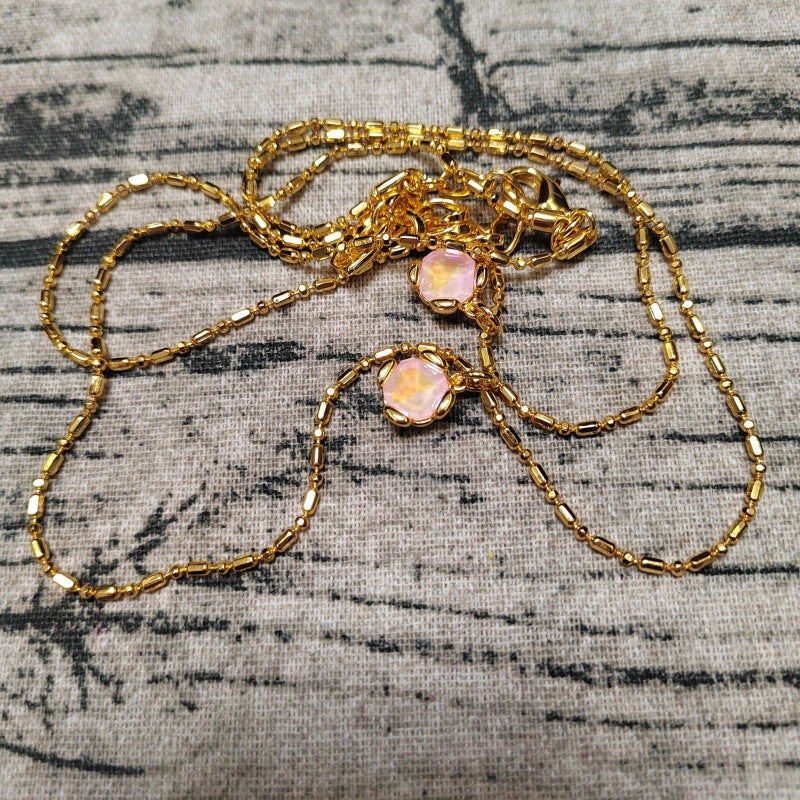 A gold chain necklace with two round, iridescent pinkish-orange cabochon gemstones, displayed on a textured gray fabric background.
