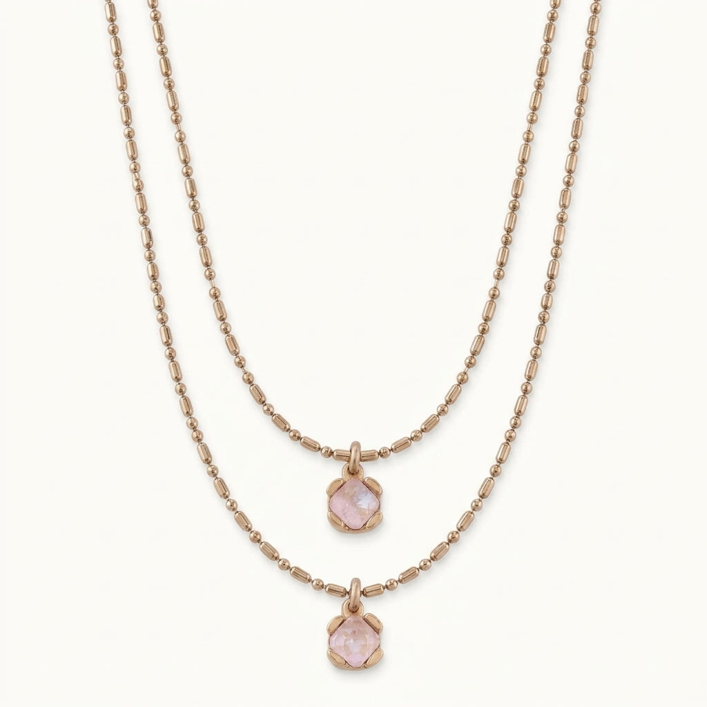 A double-strand rose gold necklace set featuring one chain with a small hexagonal pink gemstone pendant and another with a larger matching pendant, displayed on a clean off-white background.