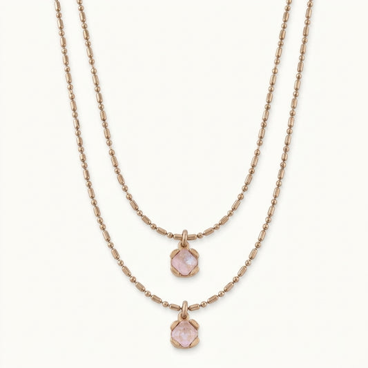 A double-strand rose gold necklace set featuring one chain with a small hexagonal pink gemstone pendant and another with a larger matching pendant, displayed on a clean off-white background.