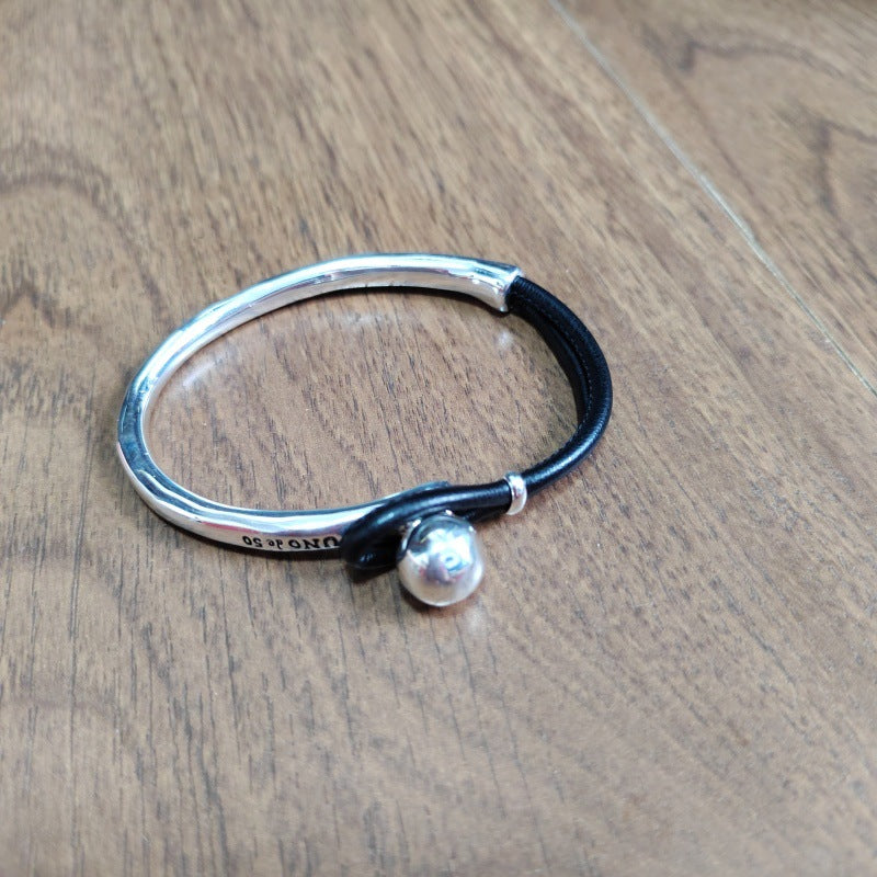 Silver bracelet with a black cord and silver bead on a wooden surface