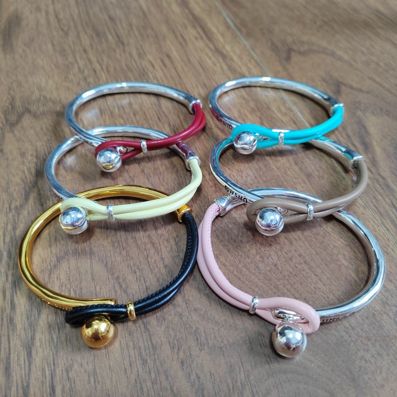 Six adjustable bangle bracelets with silver-tone metal cuffs and small metallic beads, arranged on a wooden surface. The bands are shown in silver, red, turquoise, cream, black, and pink.