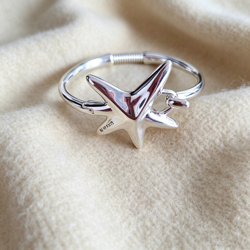 A sterling silver ring featuring a starfish design with a small seahorse nestled inside, resting on a soft, textured beige fabric background.