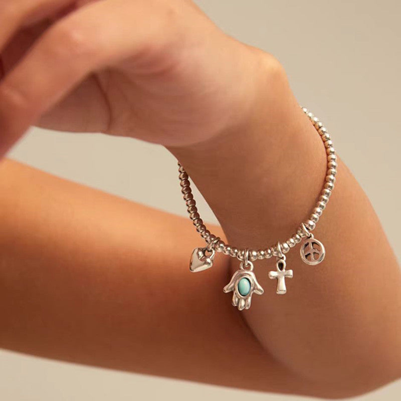 Silver bracelet with charms on a wrist against a neutral background