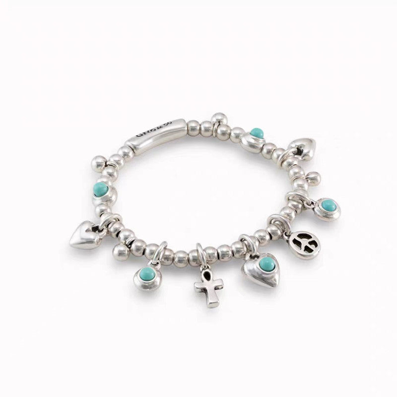 A sterling silver charm bracelet with small round beads, turquoise stone accents, and multiple dangling charms including hearts, an anchor, a peace sign, and a small cross, shown on a plain white background.
