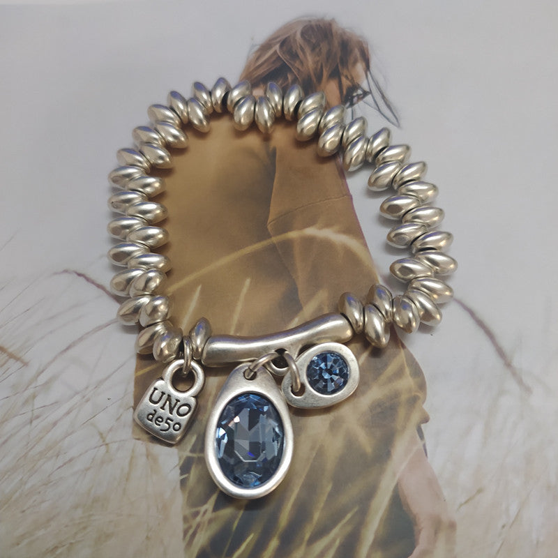 Bracelet on neutral background. Alt: “UNOde50 Bracelet with Blue Crystal Charms.”