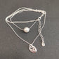 A layered silver necklace featuring a delicate chain with a single white pearl bead and a polished silver padlock pendant, displayed on a dark gray textured background.
