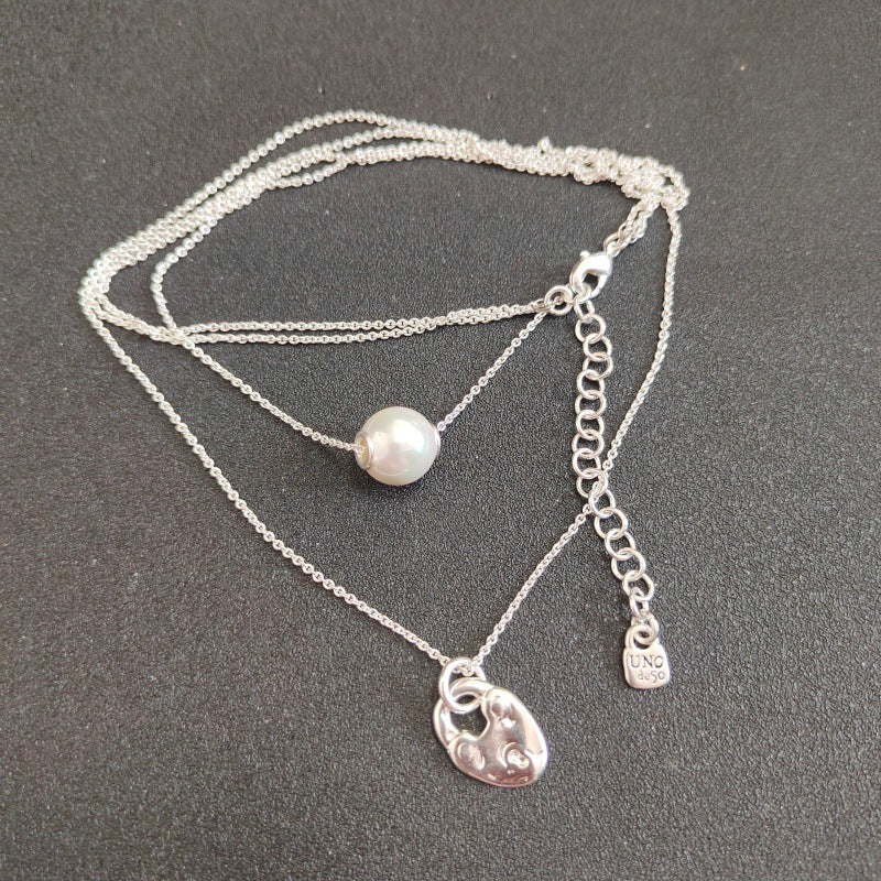 A layered silver necklace featuring a delicate chain with a single white pearl bead and a polished silver padlock pendant, displayed on a dark gray textured background.