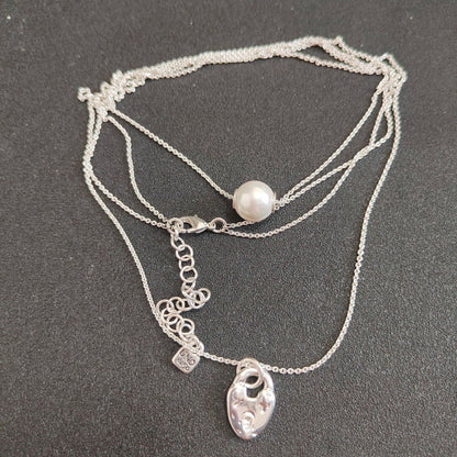 A multi-strand silver necklace featuring a single white pearl bead and a silver heart-shaped pendant, displayed on a dark gray textured background.
