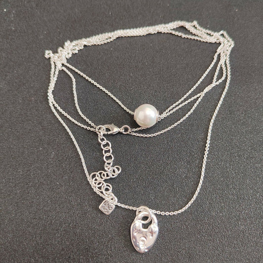 A multi-strand silver necklace featuring a single white pearl bead and a silver heart-shaped pendant, displayed on a dark gray textured background.