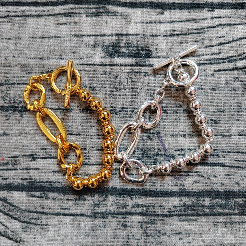 Two toggle clasp bracelets, one gold and one silver, displayed on a gray textured fabric background.