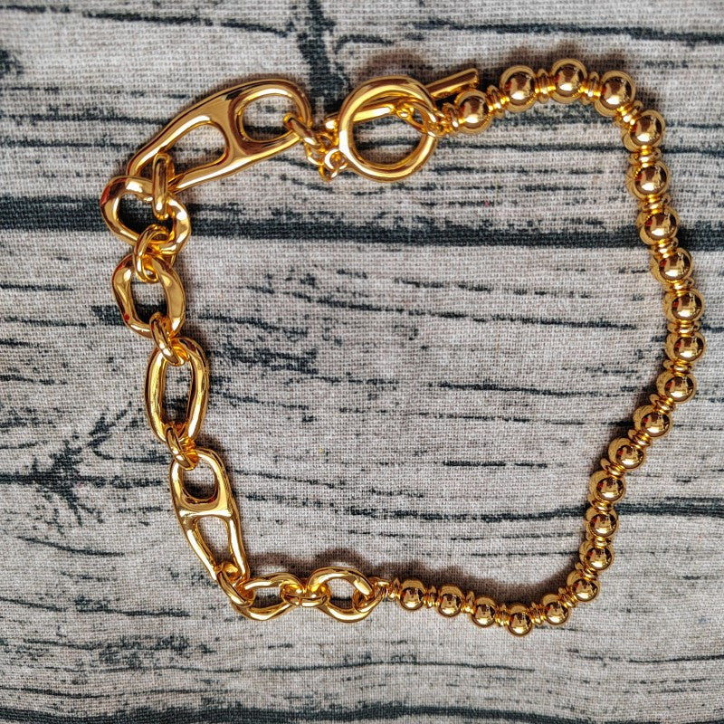 A gold-toned chain bracelet featuring a mix of chunky oval links, lobster clasp closures, and a beaded section, displayed on a gray textured fabric background.