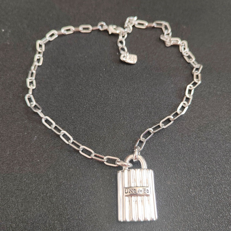 A silver chain bracelet with a lock-shaped pendant engraved with 'UNICO', displayed on a dark textured background.