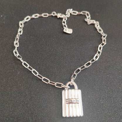A silver chain bracelet with a lock-shaped pendant engraved with 'UNICO', displayed on a dark textured background.