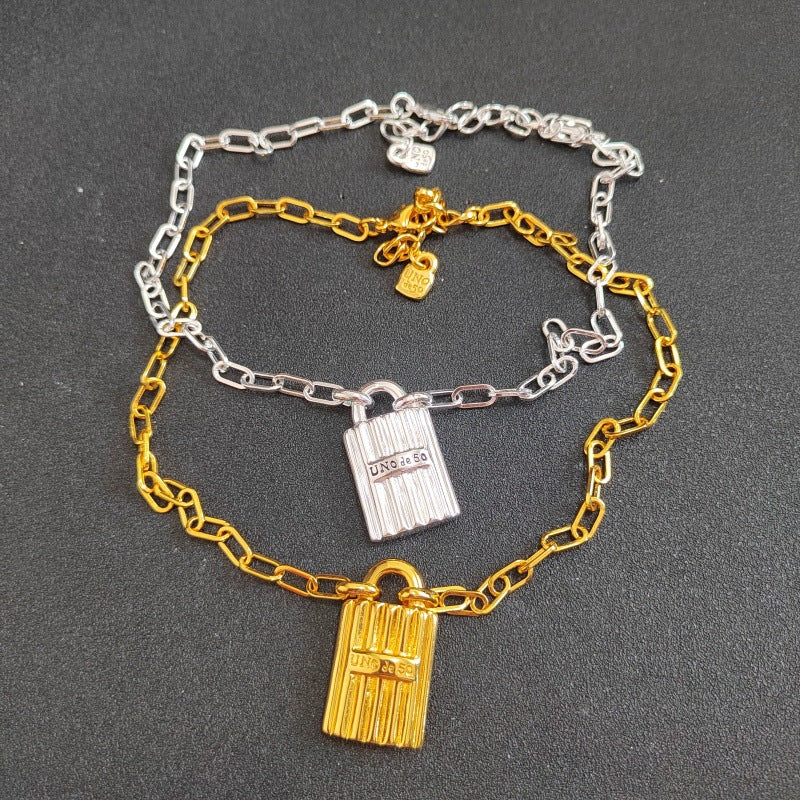 Two delicate chain necklaces, one in silver and one in gold, each featuring a miniature door-shaped pendant. The necklaces are arranged on a dark gray textured background.