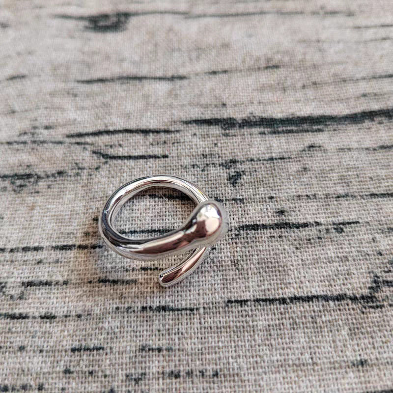 A polished silver-toned metal ring with a unique open, snake-like curved design, resting on a textured beige linen fabric background.