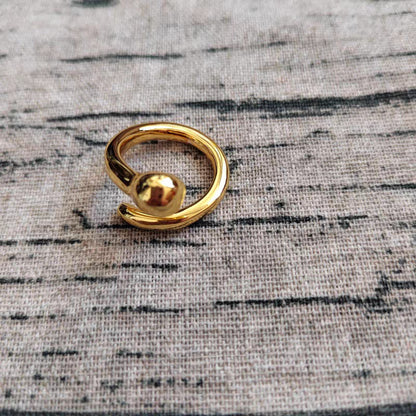 A gold-toned open ring ring with a polished spherical bead, resting on a textured gray fabric background.