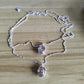 A silver beaded chain necklace with two oval pink gemstone pendants, displayed on a light wood surface.