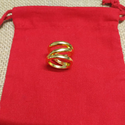 A gold ring with a twisted, overlapping band design, displayed on a bright red drawstring pouch over a beige textured fabric background.