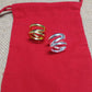 Two spiral wrap-style rings, one gold-toned and one silver-toned, displayed on a red fabric pouch over a beige woven surface.