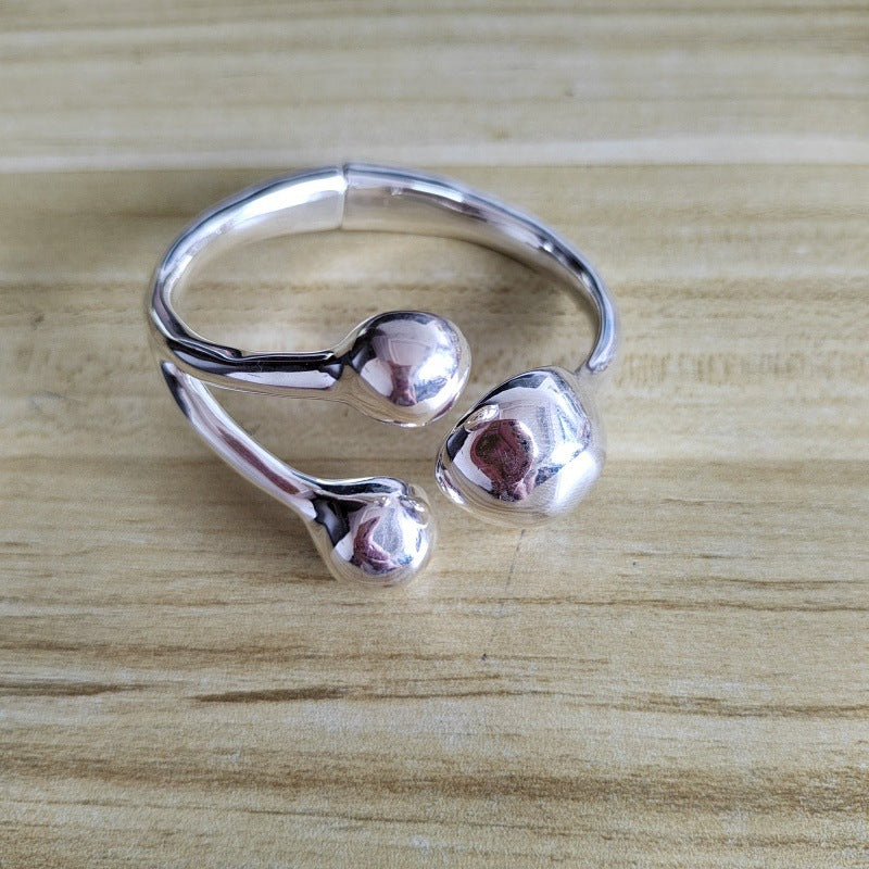 A polished silver-toned open cuff ring with three rounded bead-like protrusions, photographed on a light wood surface.