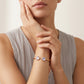 A close-up of a model wearing a rose gold cuff bracelet with two heart-shaped clear gemstones on her wrist, paired with a ribbed taupe top against a soft beige background.