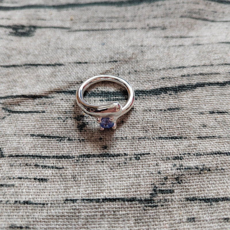 A silver ring with a small round purple gemstone, resting on a textured gray fabric background.