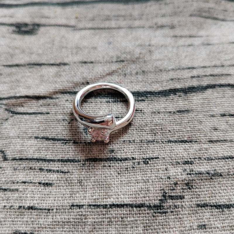 A silver cat-shaped ring with a small clear gemstone, resting on a textured beige linen fabric background.