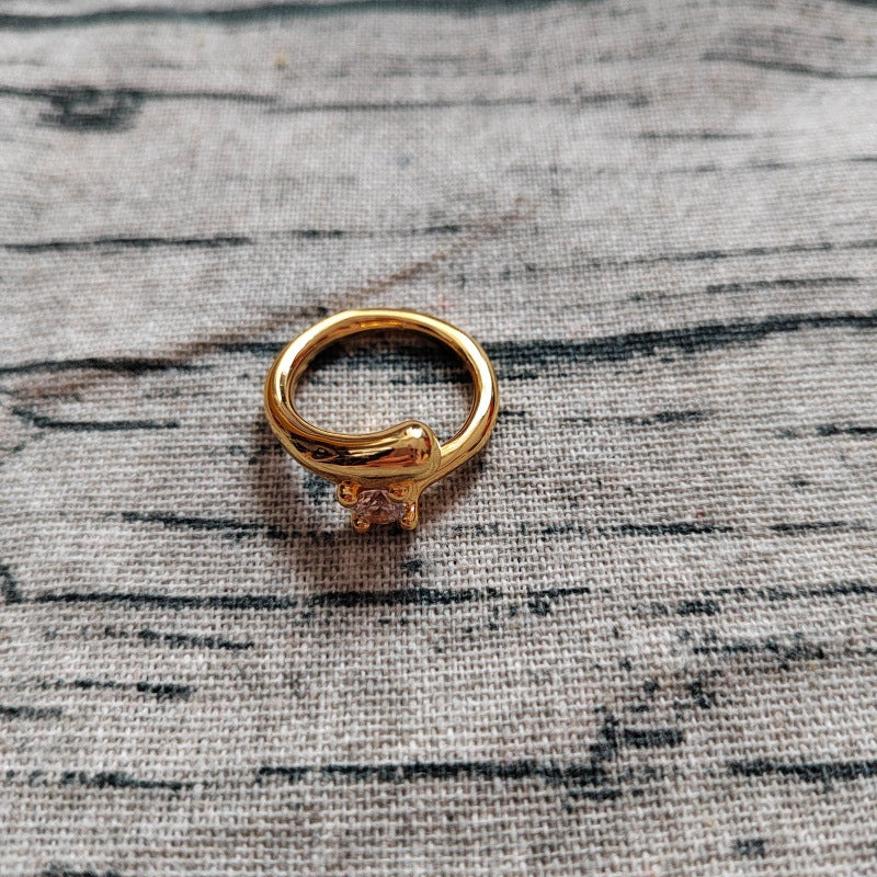 A gold ring with a small clear gemstone in a prong setting, resting on a textured gray fabric background.
